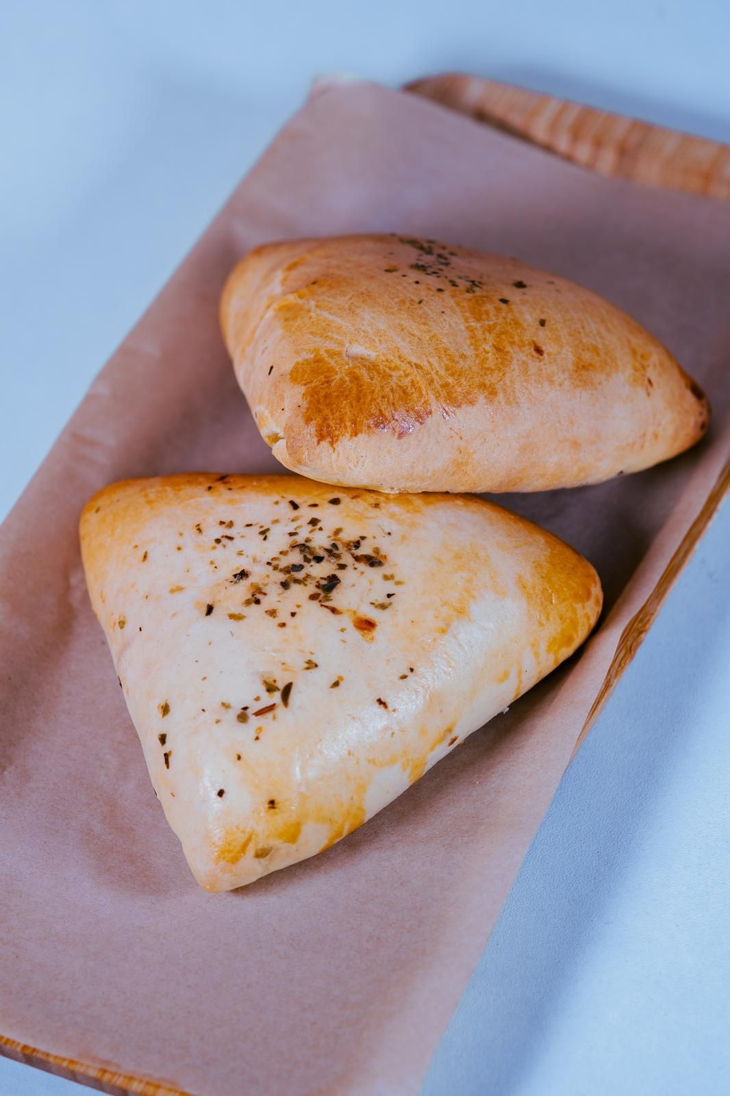 Dos pasteles horneados de color dorado cubiertos con hierbas sobre papel pergamino.