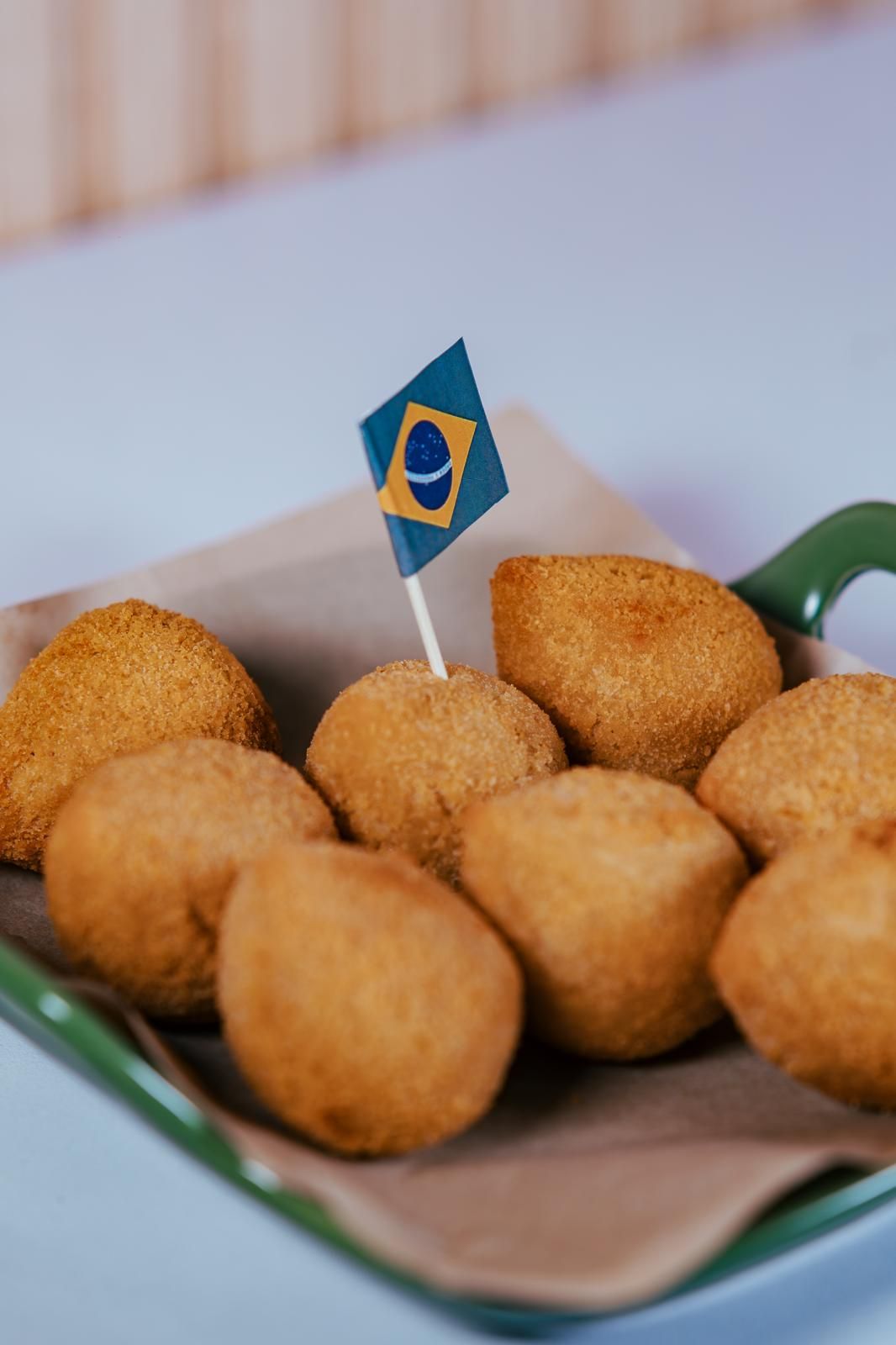 Aperitivos brasileños fritos (coxinha) en una bandeja con un palillo con la bandera brasileña.