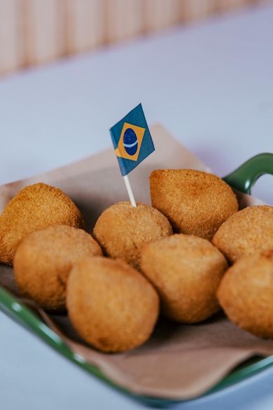 Una ración de coxinha dorada como aperitivo en un plato verde, adornada con un pequeño palillo que representa la bandera de Brasil.