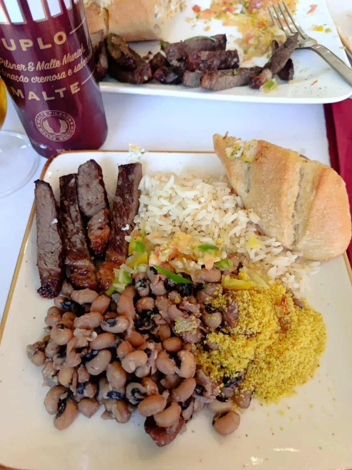 Plato con carne a la parrilla, frijoles de ojo negro, arroz, pan y cerveza.
