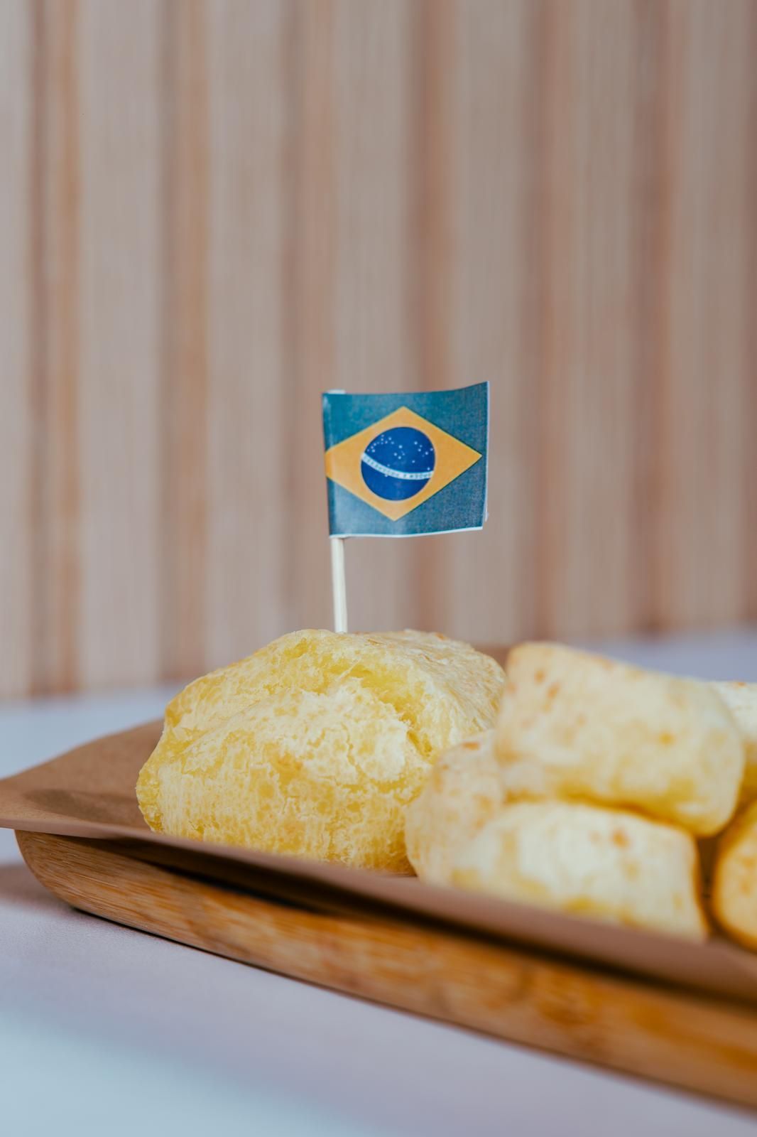 Pan de queso, servido en una bandeja de madera con un palillo con la bandera brasileña.