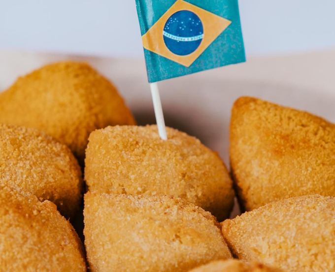 Un grupo de coxinhas brasileñas de color marrón dorado y con forma de lágrima, una de ellas perforada con una pequeña bandera de Brasil.