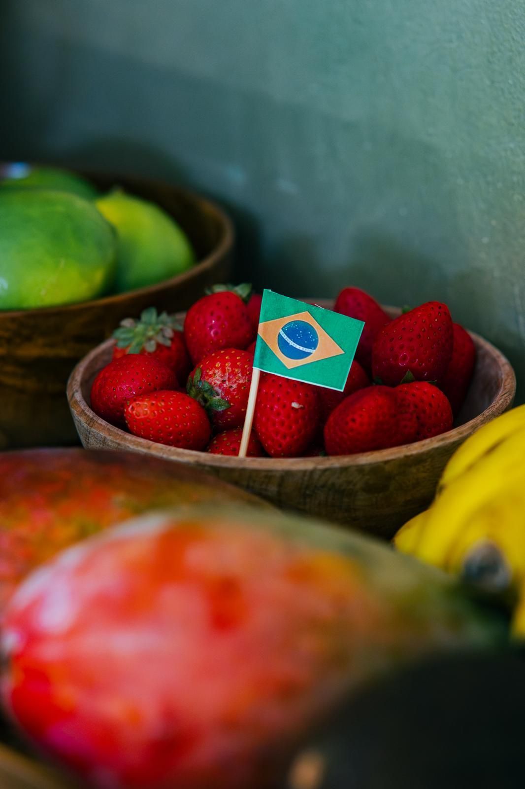 Cuenco de fresas con bandera brasileña, otras frutas en el fondo.