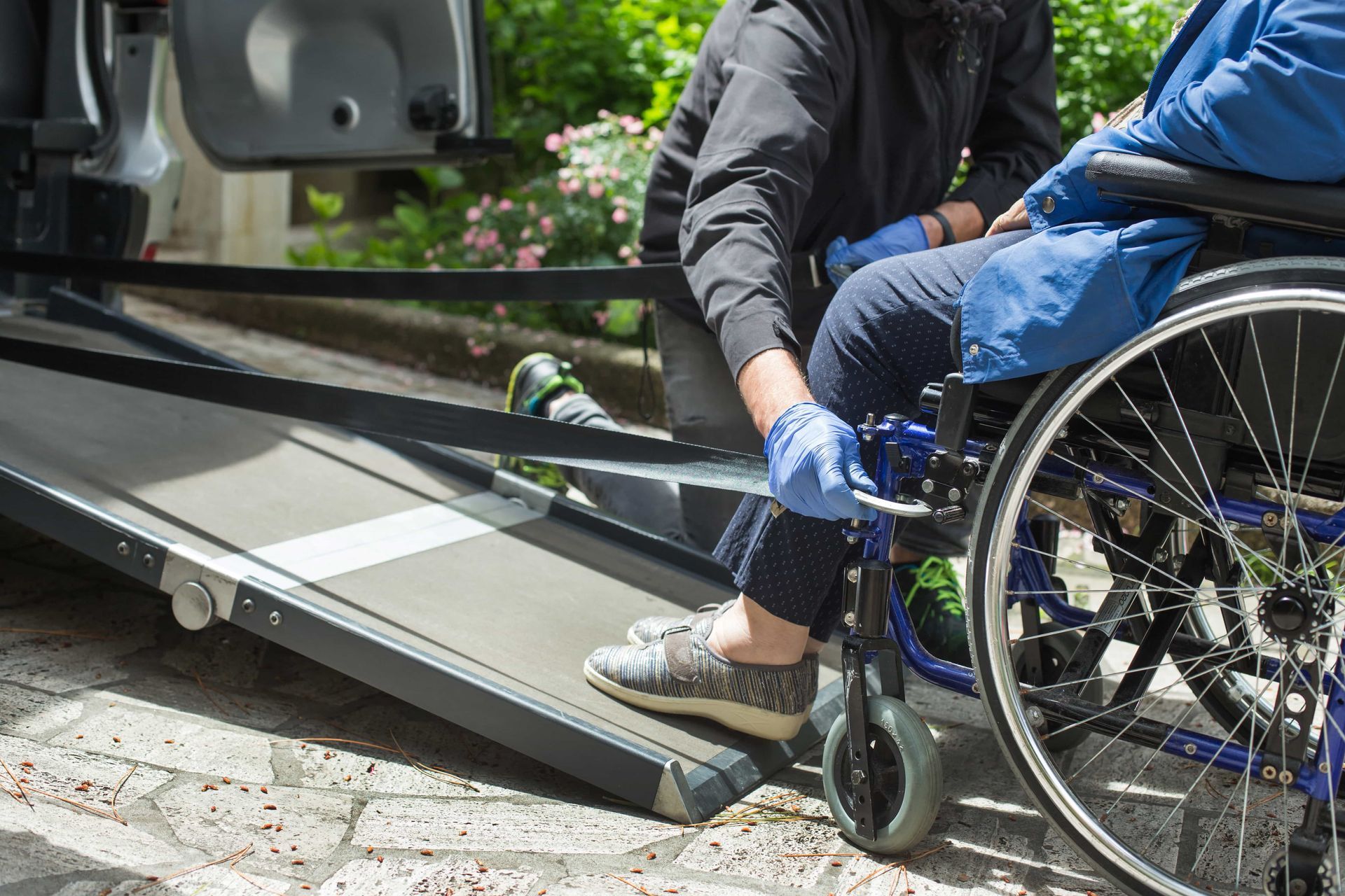 une personne en fauteuil roulant est aidé par une personne pour monter dans un véhicule grâce à une rampe d'accès