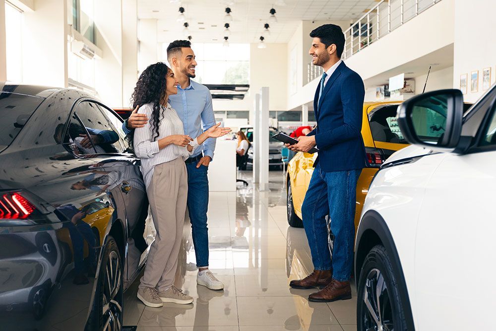 Ein Mann und eine Frau unterhalten sich in einem Autohaus mit einem Autoverkäufer.