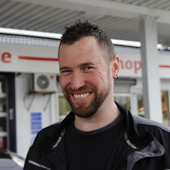 Ein Mann lächelt vor einem Schild mit der Aufschrift „Stopp“