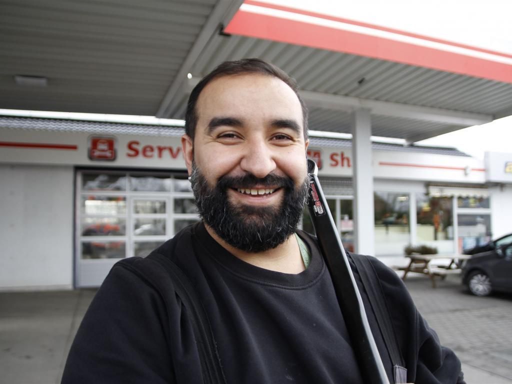 Ein Mann mit Bart lächelt vor einer Tankstelle