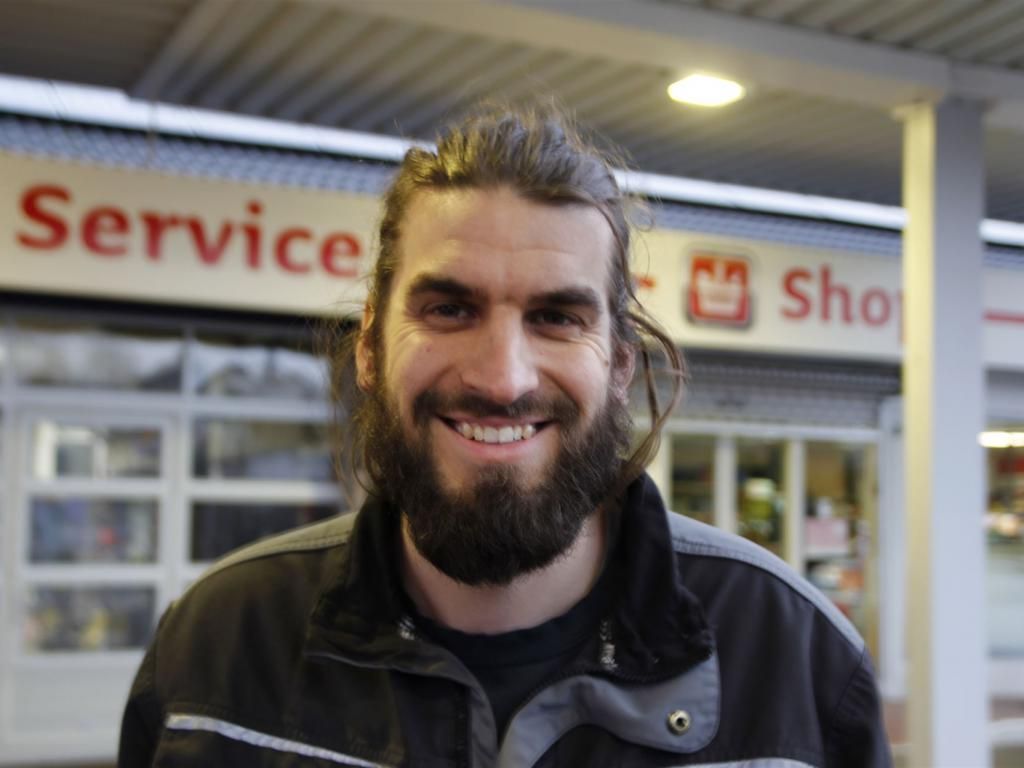 Ein Mann mit Bart lächelt vor einer Werkstatt