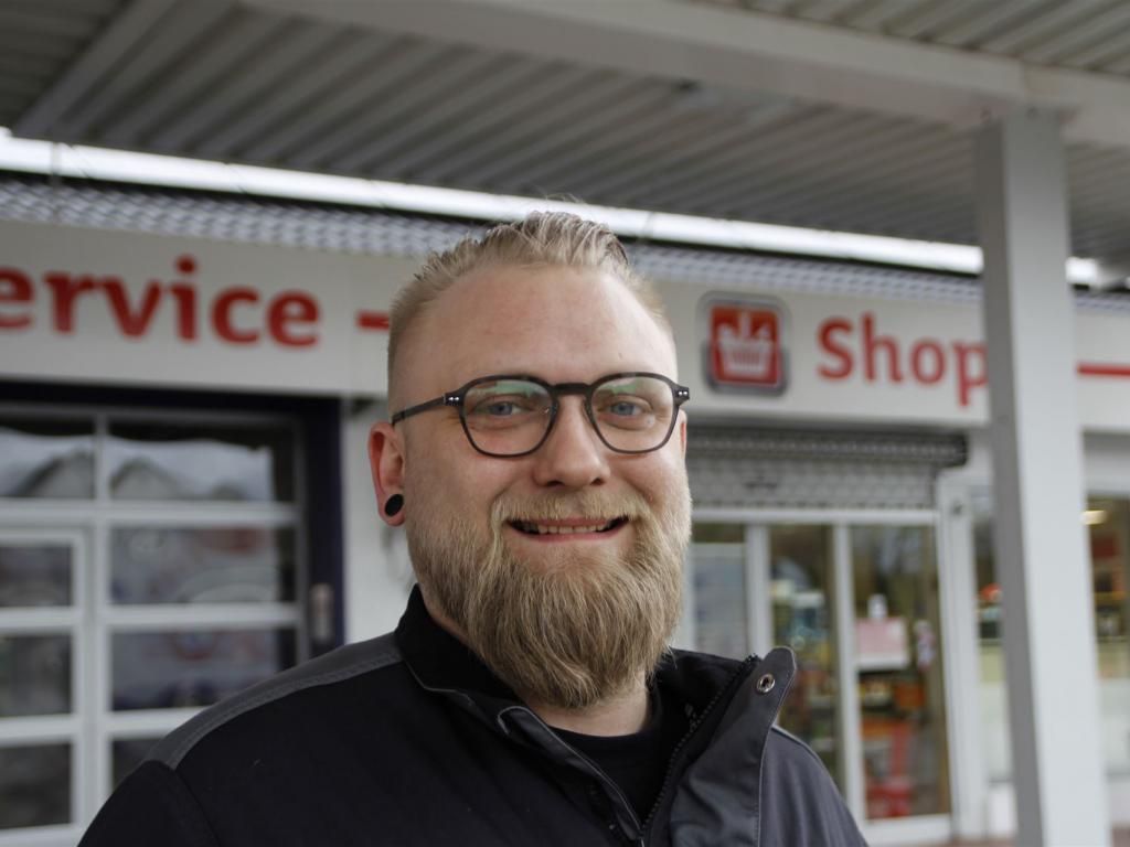 Ein Mann mit Bart und Brille steht vor einer Werkstatt.