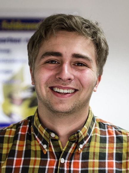 Ein junger Mann in einem karierten Hemd lächelt in die Kamera