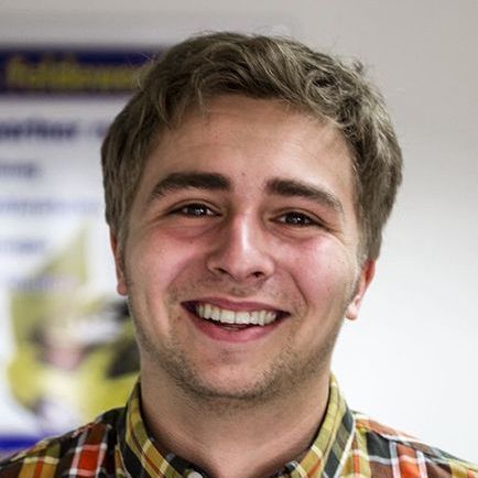 Ein junger Mann in einem karierten Hemd lächelt in die Kamera.