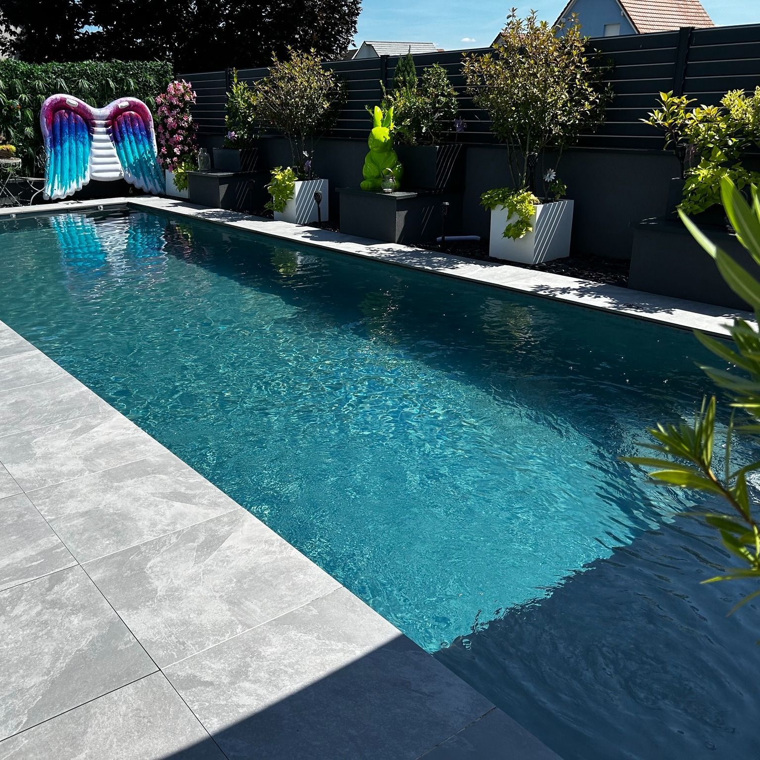 Piscine moderne près d'une haie et avec des décorations.