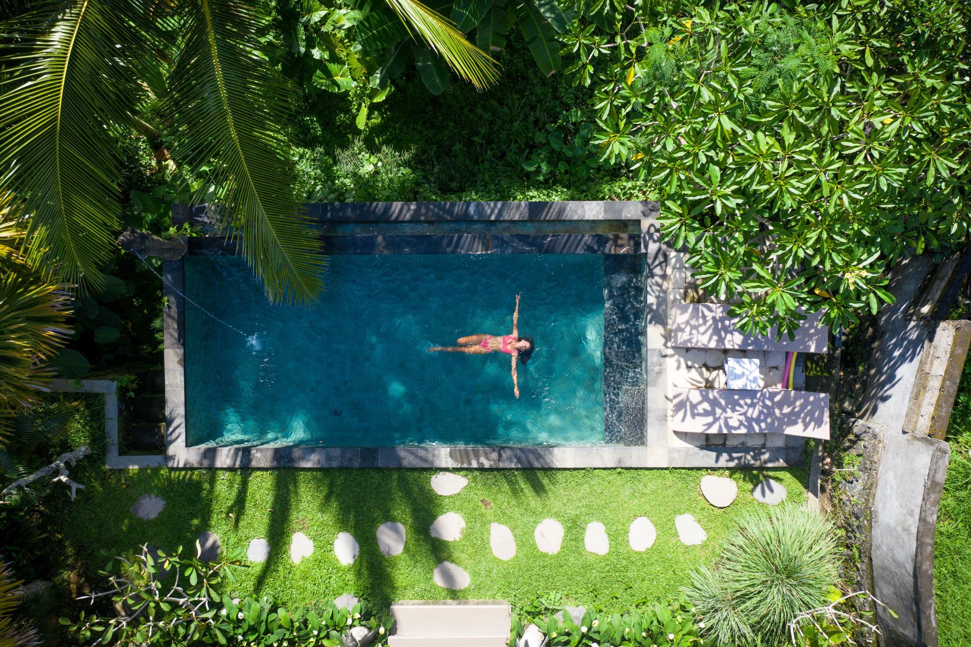 Femme qui se baigne dans une piscine entourée de végétation vue de haut.