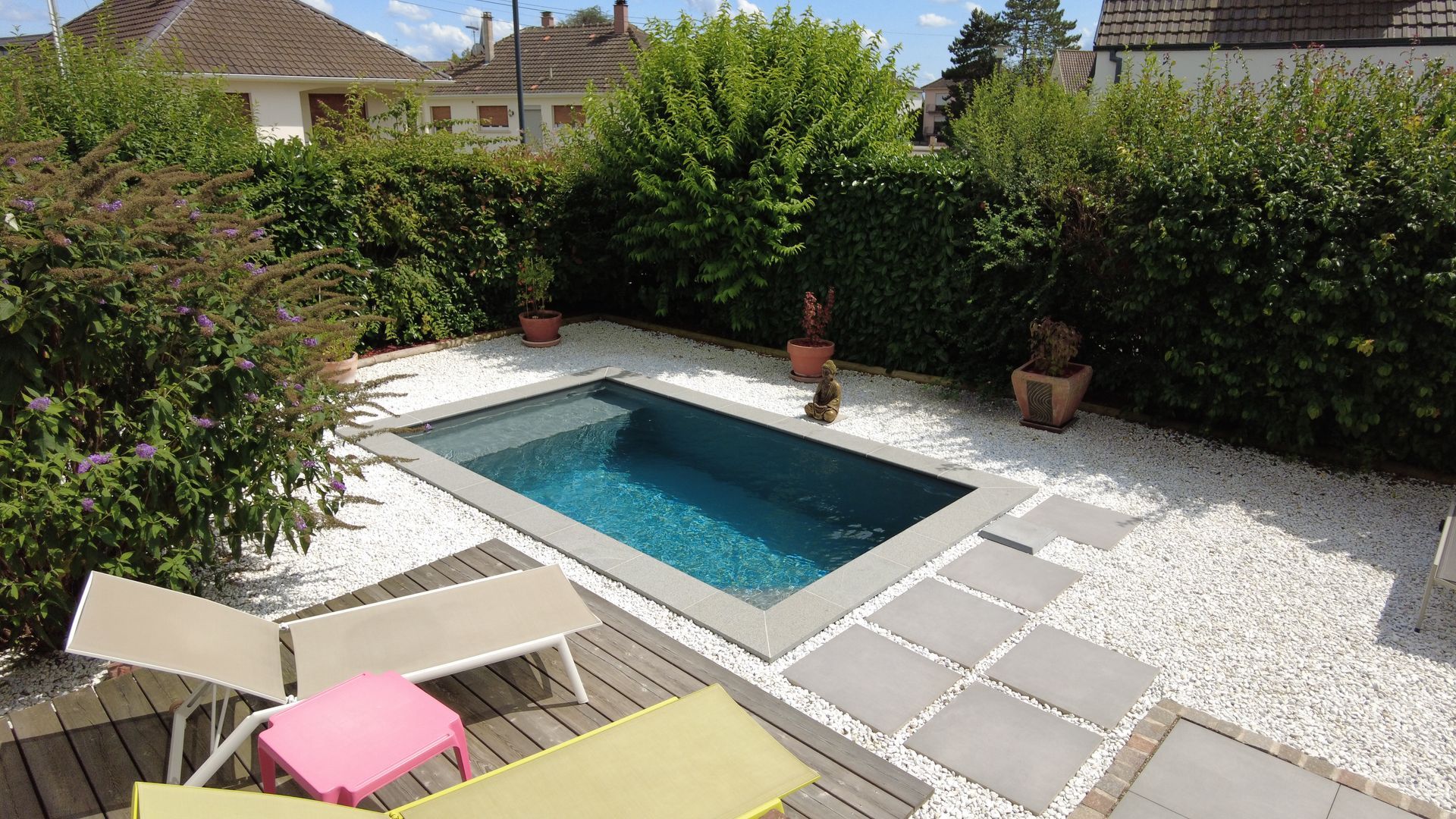 Dalles en béton permettant d'atteindre une piscine au milieu de cailloux blancs.