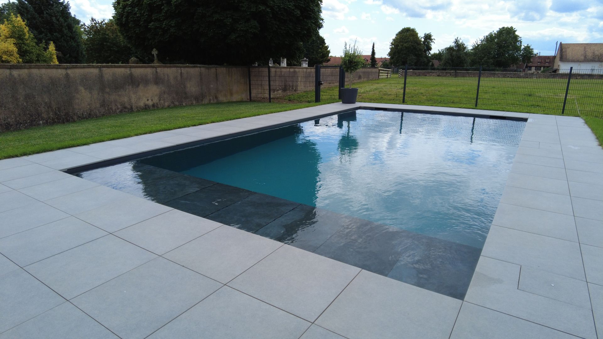 Piscine rectangulaire avec terrasse en dalles béton.