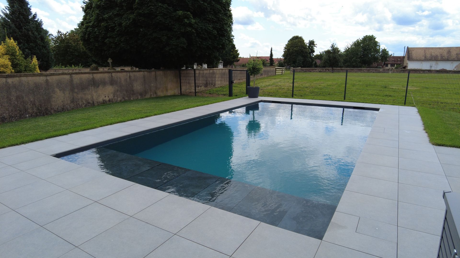 Piscine en béton avec contour en dalles grises.