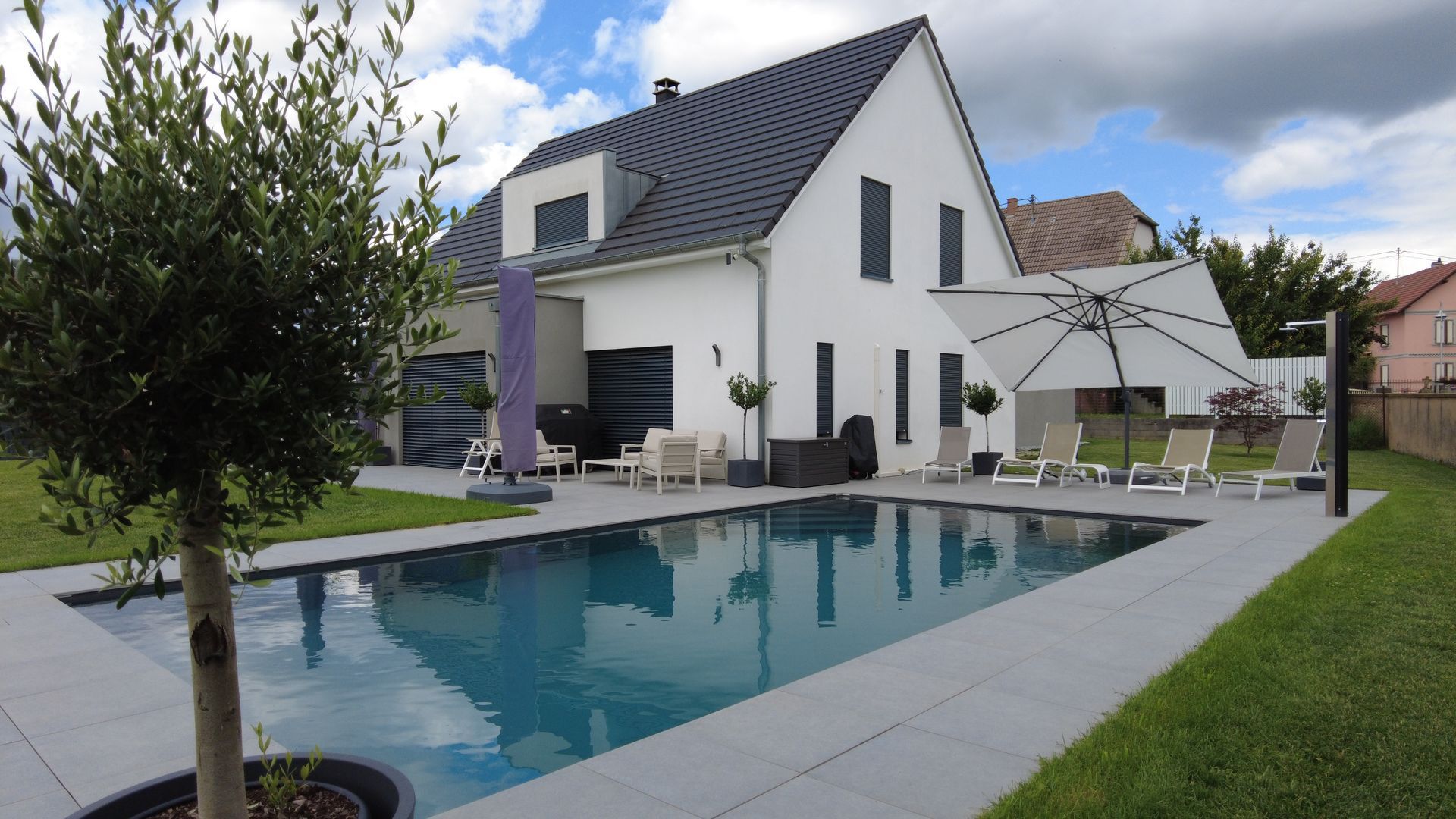 Piscine creusée avec terrasse en béton gris et des arbres en pot.