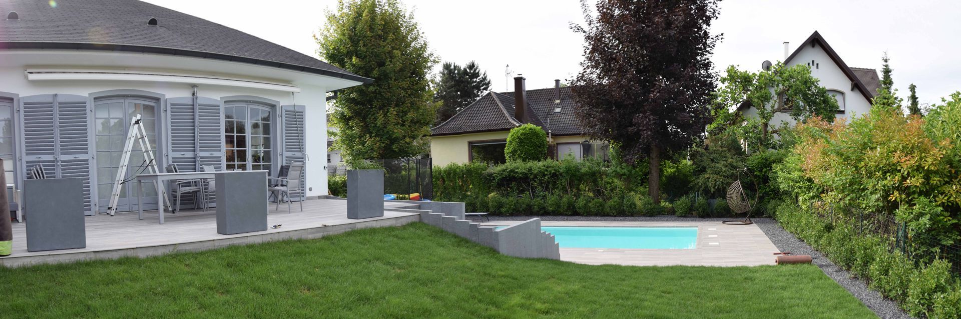 Jardin donnant sur une grande piscine reliée à une maison par un escalier en béton.