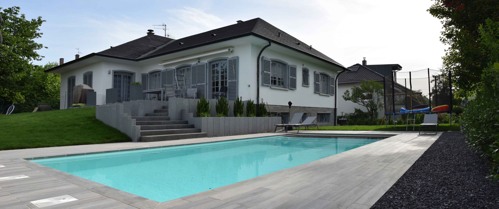 Piscine avec une grande terrasse et un espace de jeu pour des enfants.