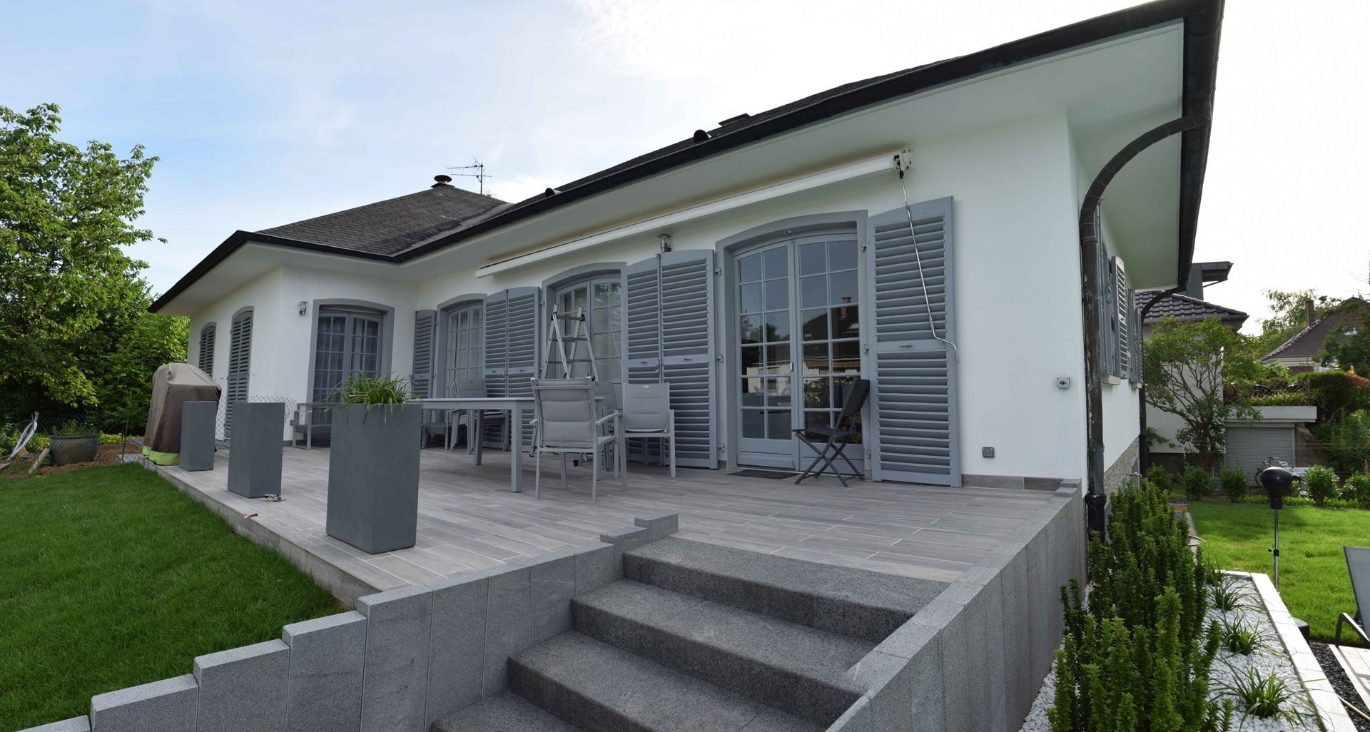 Massifs de plantes à proximité d'une terrasse et d'un escalier en béton.