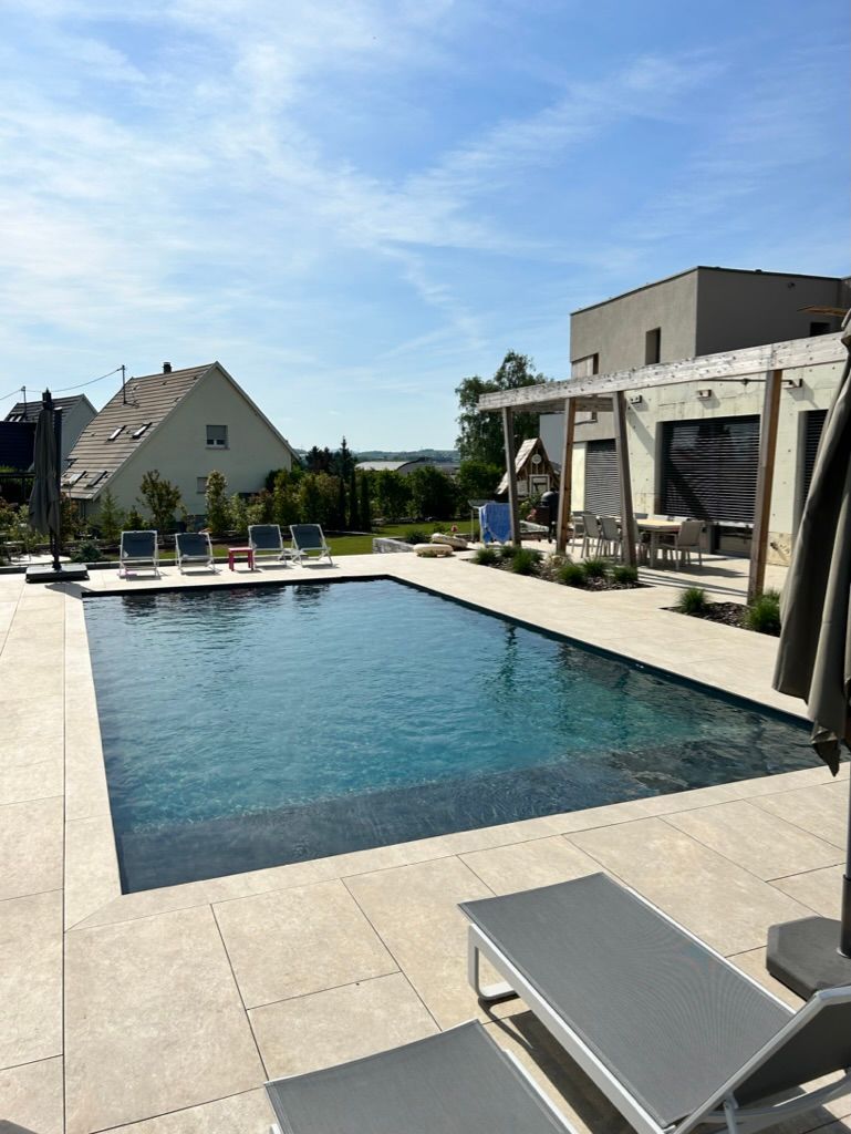 Piscine en béton avec terrasse dallée et plusieurs espaces avec des transats.