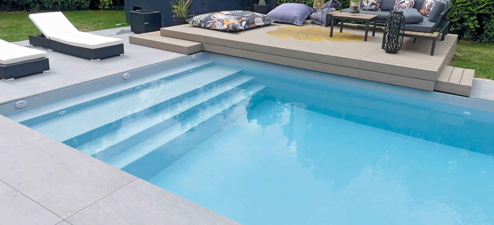 Piscine à coque avec plusieurs transats et coussins pour s'installer.