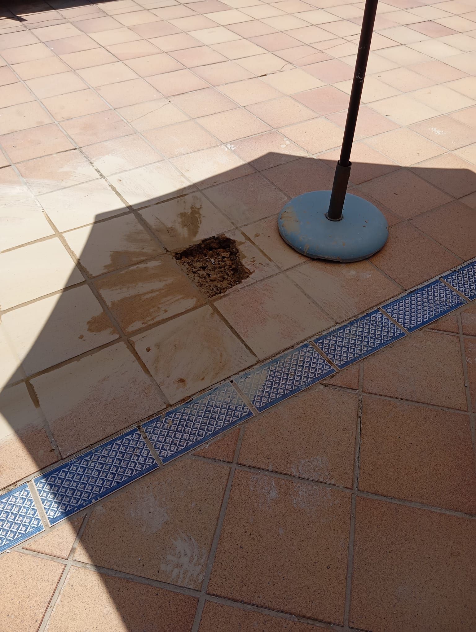 La sombra de un paraguas se proyecta sobre un suelo de baldosas.