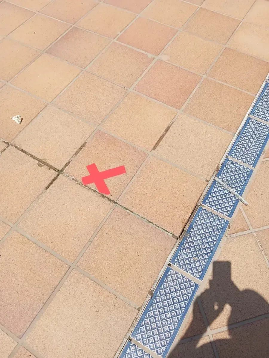 Una marca roja en forma de X sobre baldosas cuadradas de color claro, junto a un borde decorativo azul con un estampado.