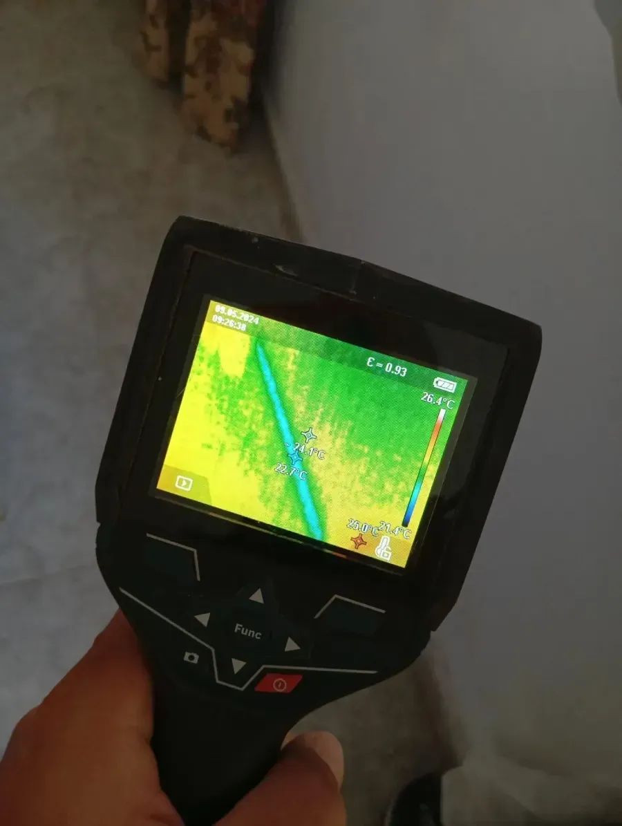 Una mano sostiene una cámara termográfica que muestra una línea vertical azul fría