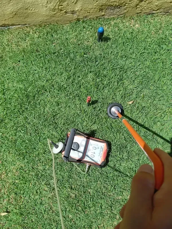 Vista en primera persona de una persona utilizando un detector de metales y un dispositivo portátil en un césped verde.