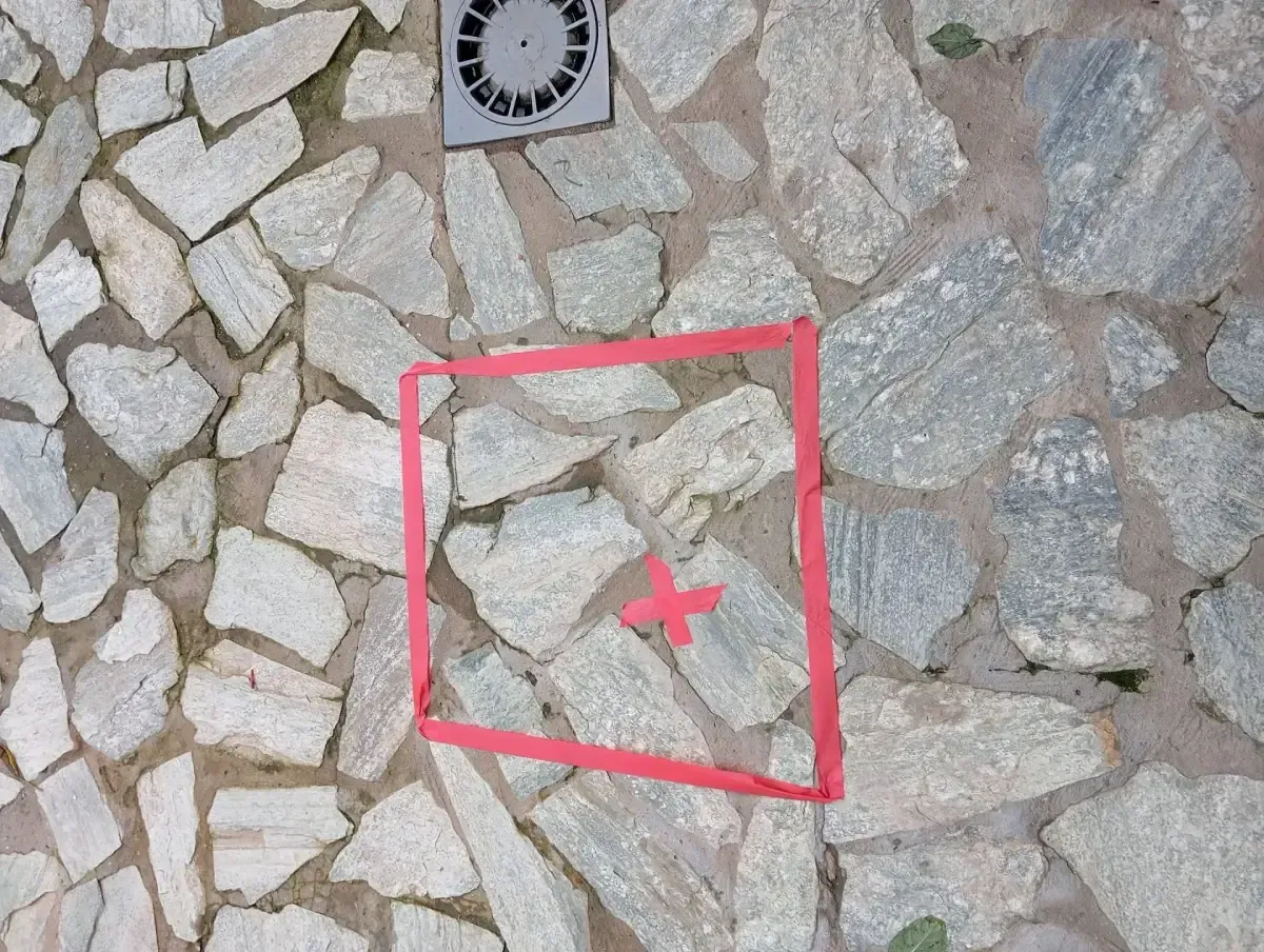 Sobre una superficie irregular de piedra de color claro, se observa un cuadrado rojo con una pequeña cruz roja en el centro.