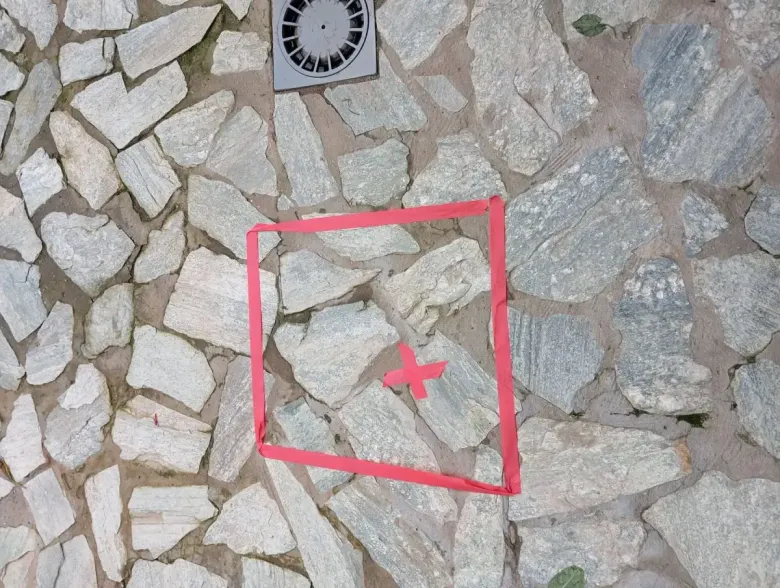 Sobre una superficie irregular de piedra de color claro, se observa un cuadrado rojo con una pequeña cruz roja en el centro.