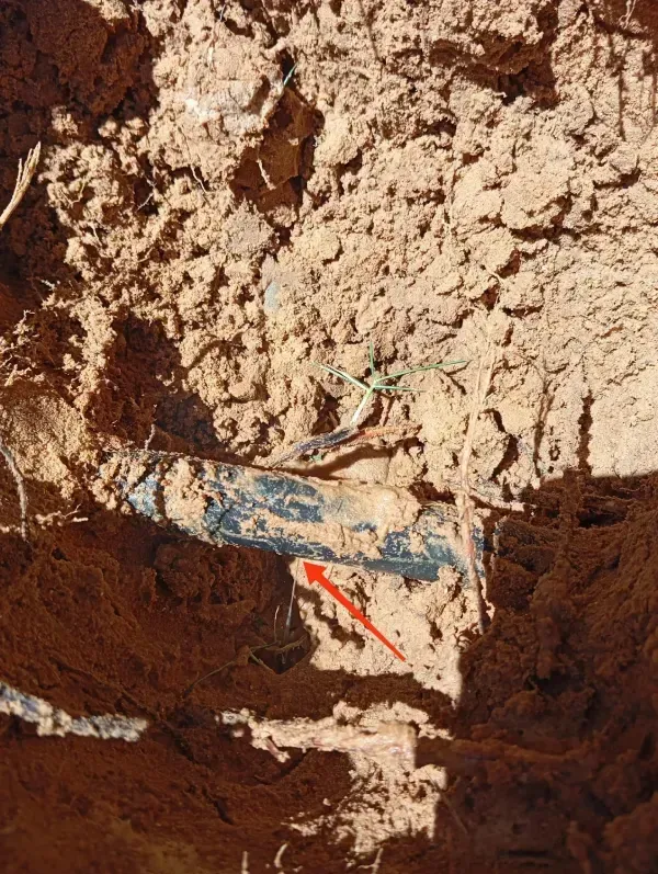 Una flecha roja señala una tubería azul parcialmente expuesta en el suelo