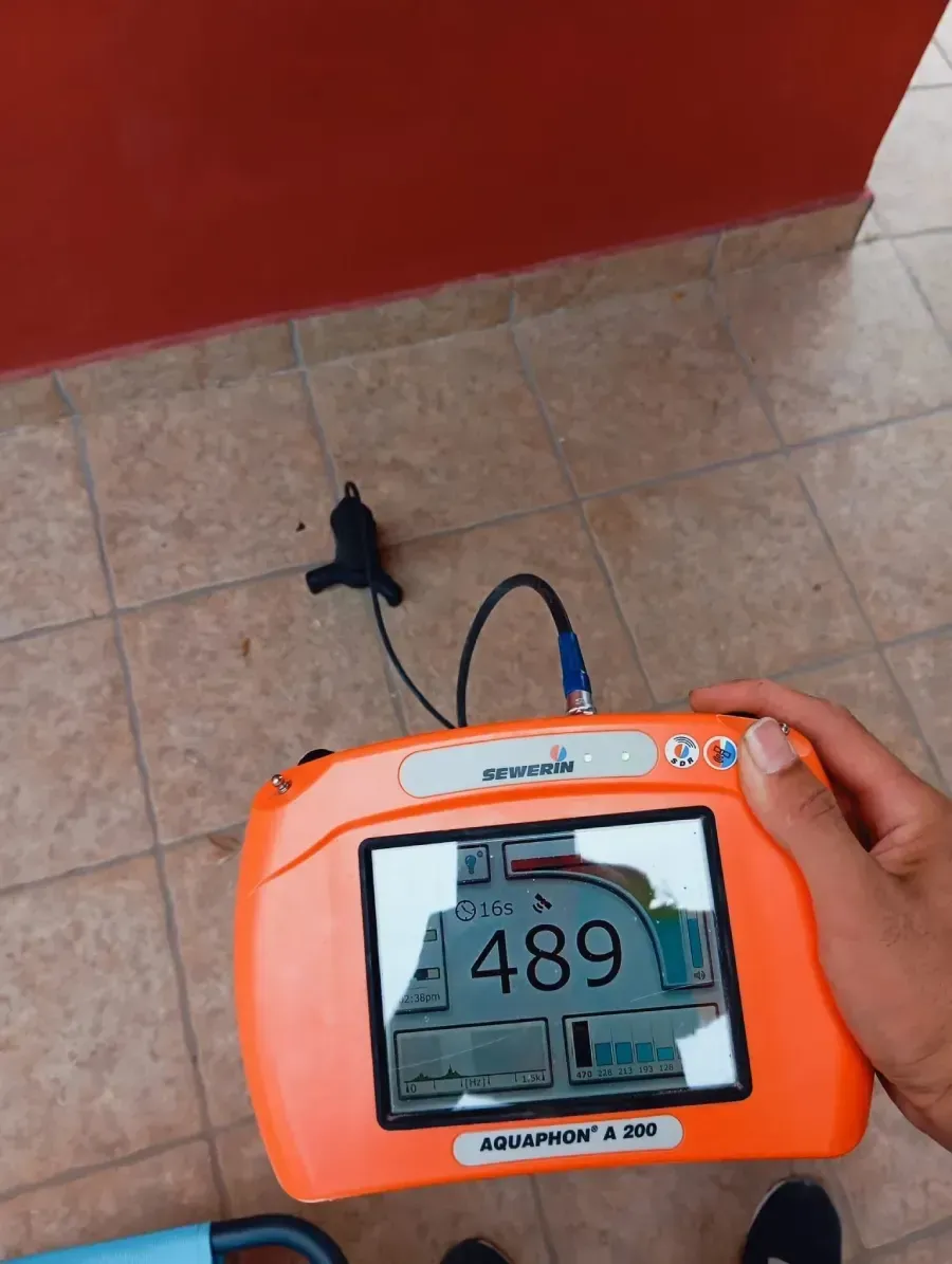 Un detector de fugas portátil de color naranja, el Aquascan 610, muestra una lectura de 489 en su pantalla