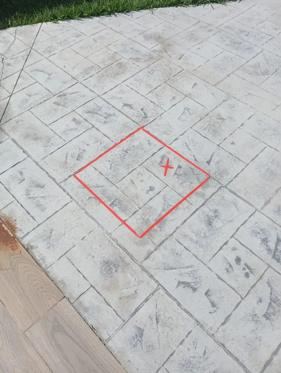 Un cuadrado rojo con una 'X' marcada en su interior, dibujado sobre una superficie de patio de hormigón gris texturizado.
