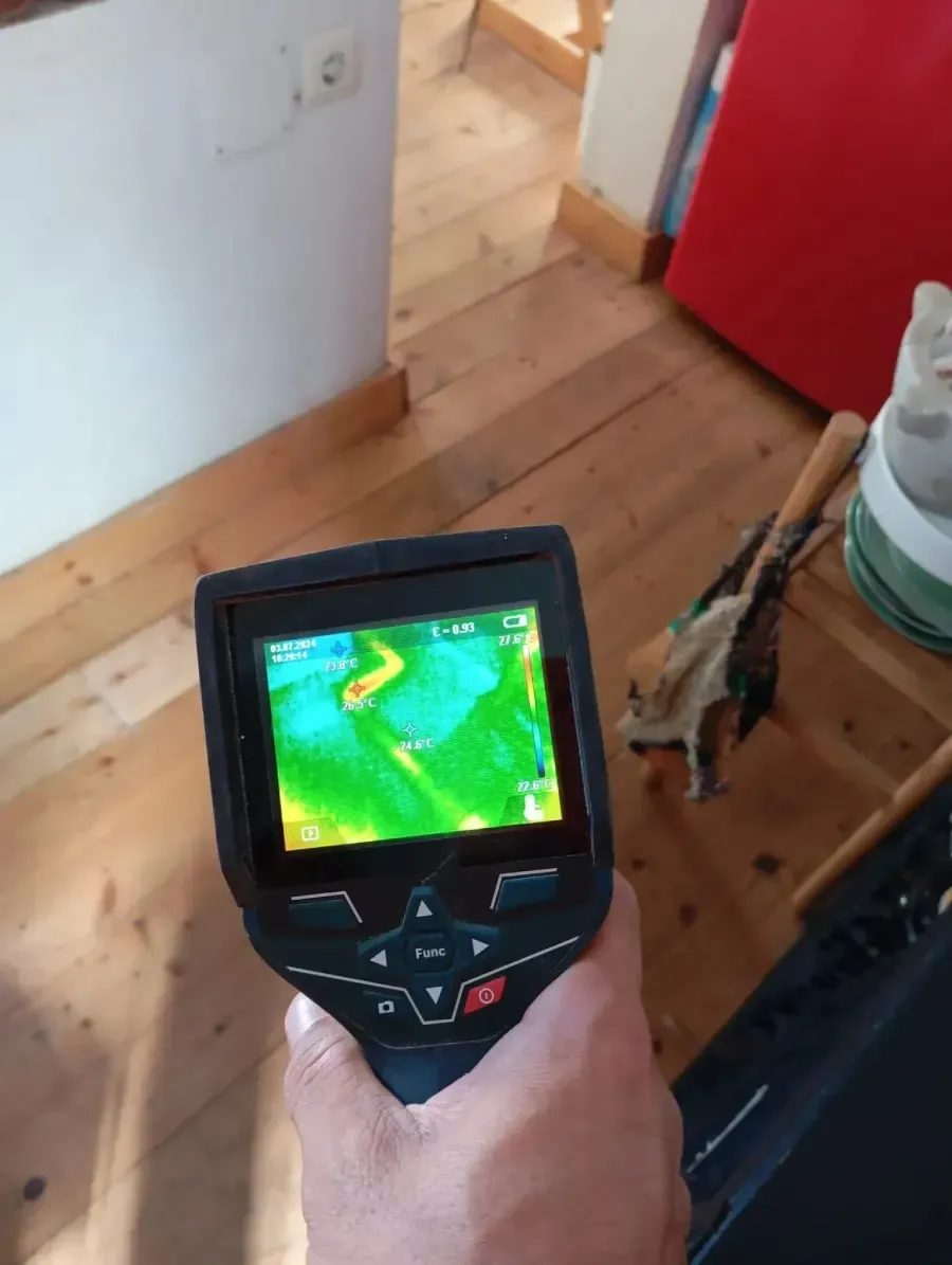 Una persona sostiene una cámara termográfica que muestra un mapa de calor de un suelo de madera