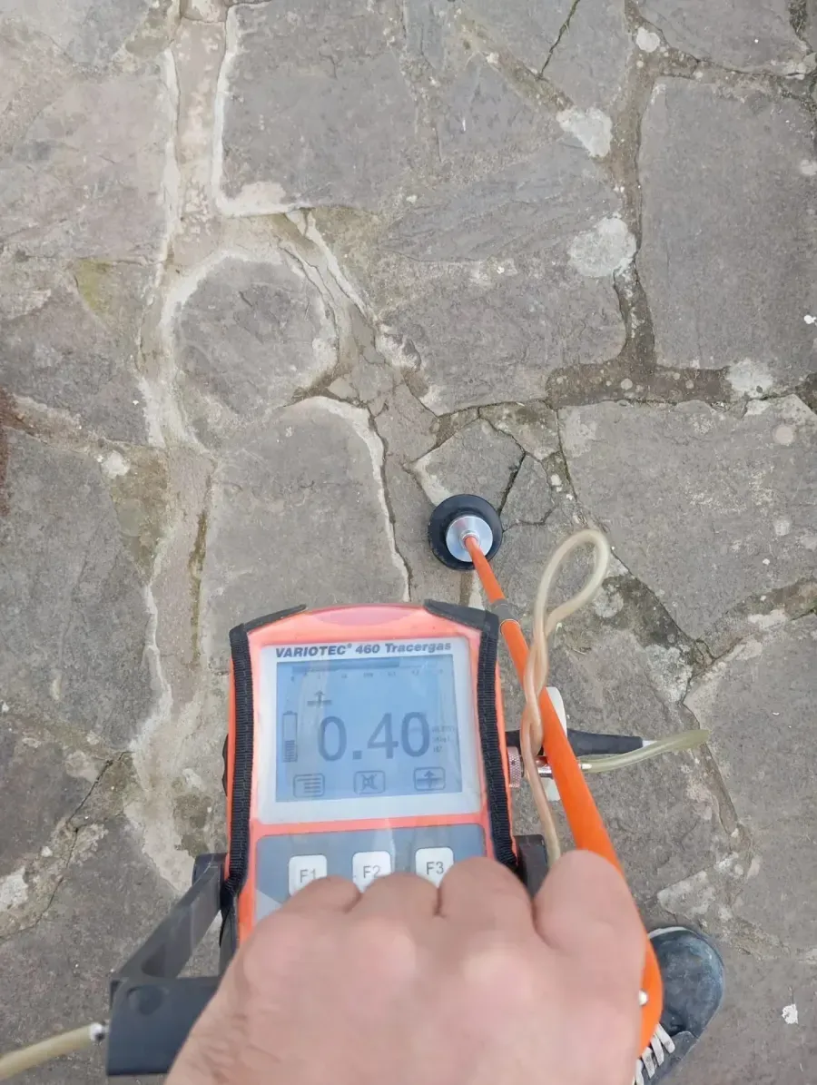 Una mano sostiene un medidor ultrasónico portátil de espesor de hormigón, midiendo una superficie pavimentada con piedra