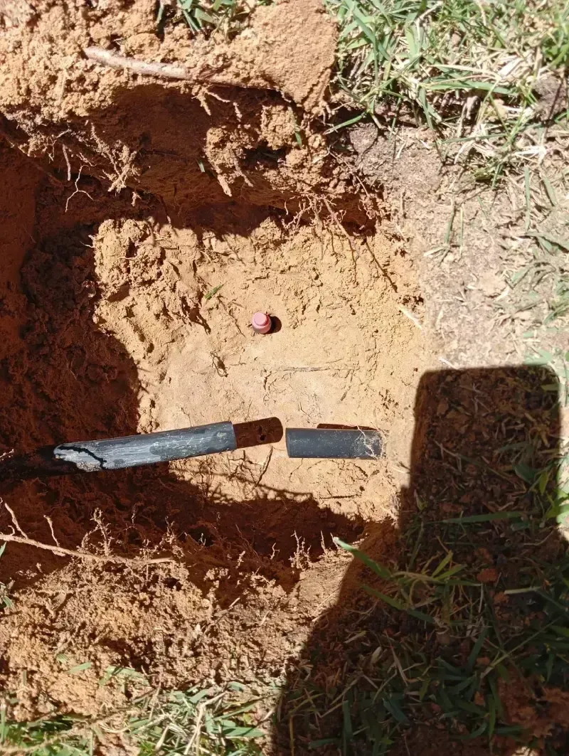 Una tubería de riego negra y rota descansa en un agujero cuadrado excavado en tierra roja