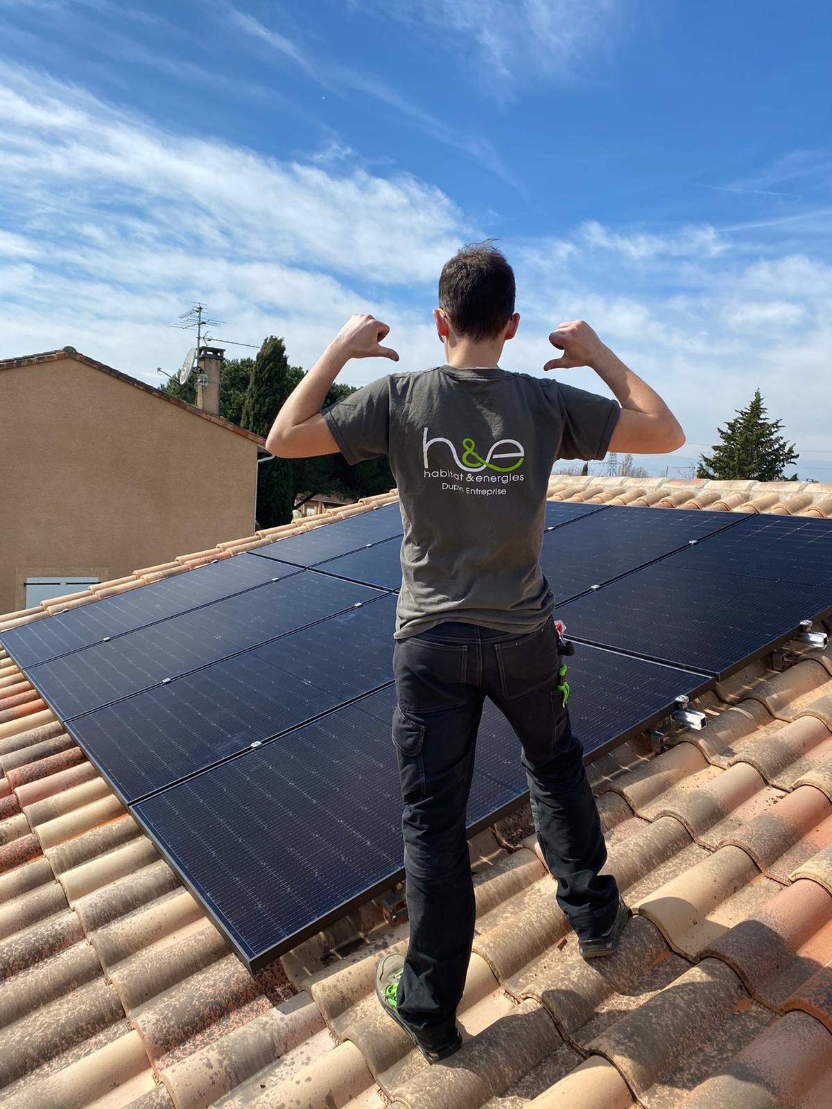 Un homme sur un toit avec des panneaux solaires, pointant les pouces vers le bas ; journée ensoleillée.