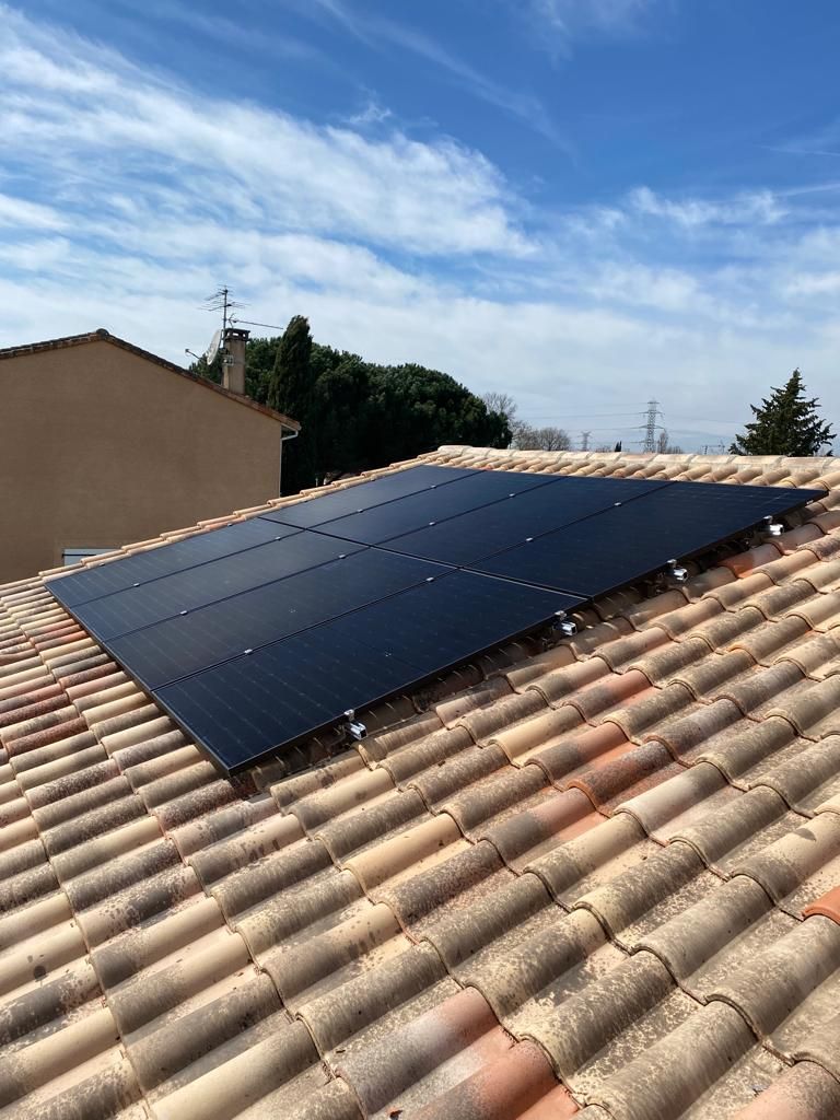 Panneaux solaires installés sur un toit en tuiles en terre cuite contre un ciel bleu.