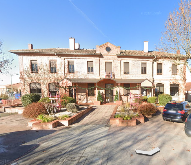 Bâtiment en briques de deux étages avec rampe et aménagement paysager, probablement un bâtiment public. Journée ensoleillée.