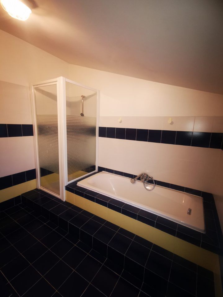 Salle de bain avec carrelage noir et jaune, murs blancs, une cabine de douche et une baignoire.