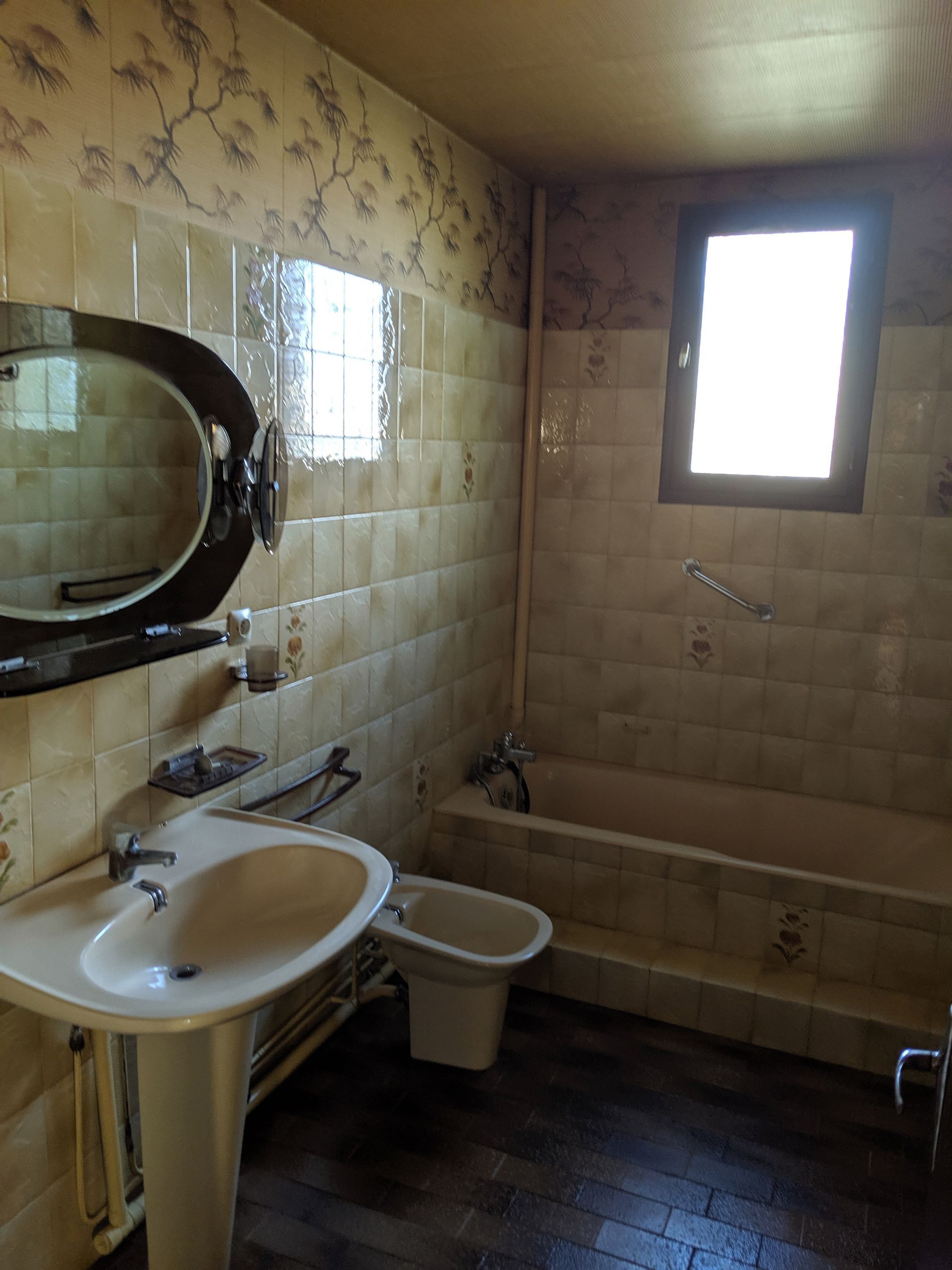 Salle de bain avec lavabo blanc, toilettes et baignoire ; murs carrelés crème avec bordure de papier peint à motifs.