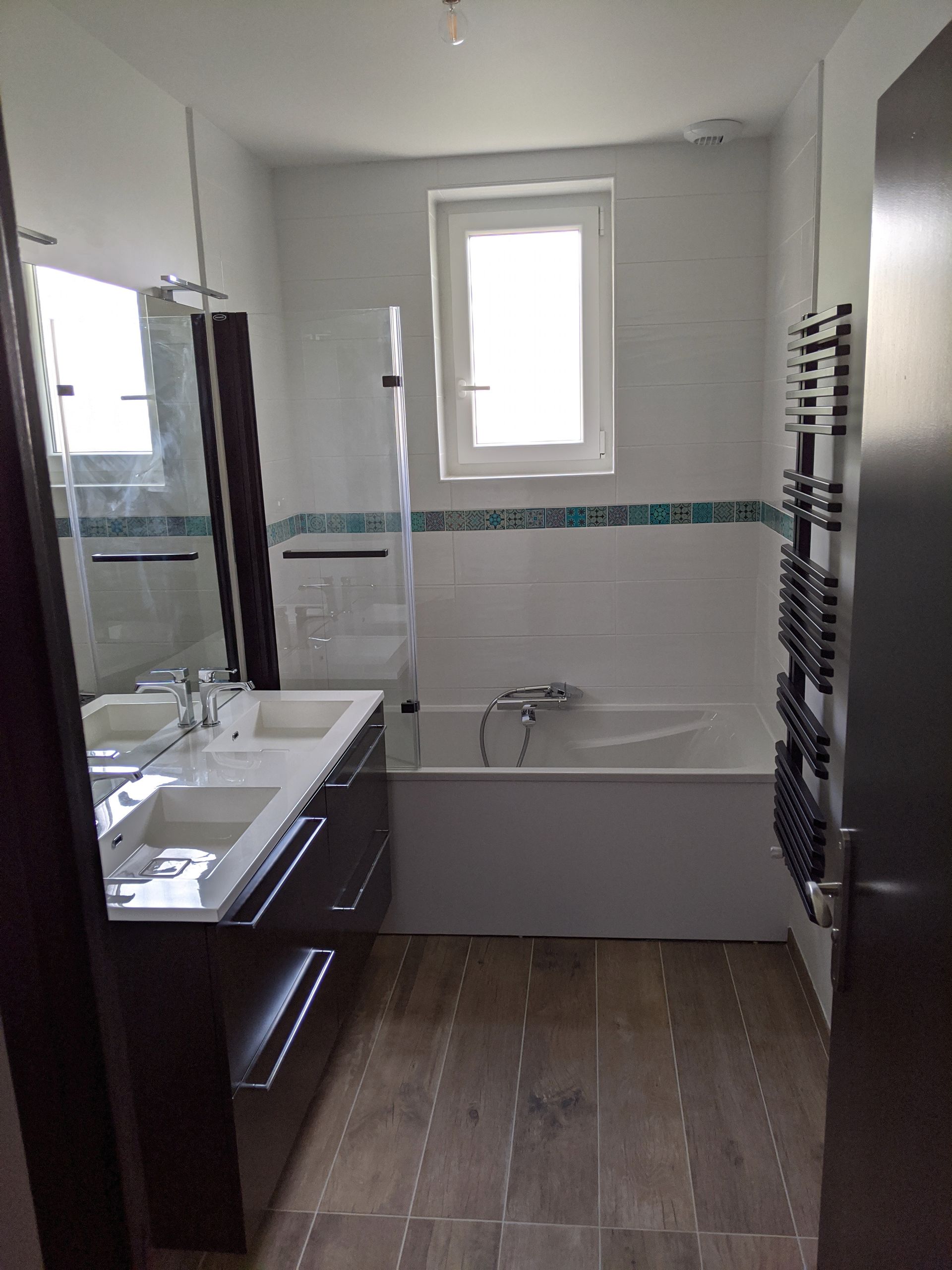 Salle de bain moderne avec baignoire, double vasque, sol imitation bois et sèche-serviettes.