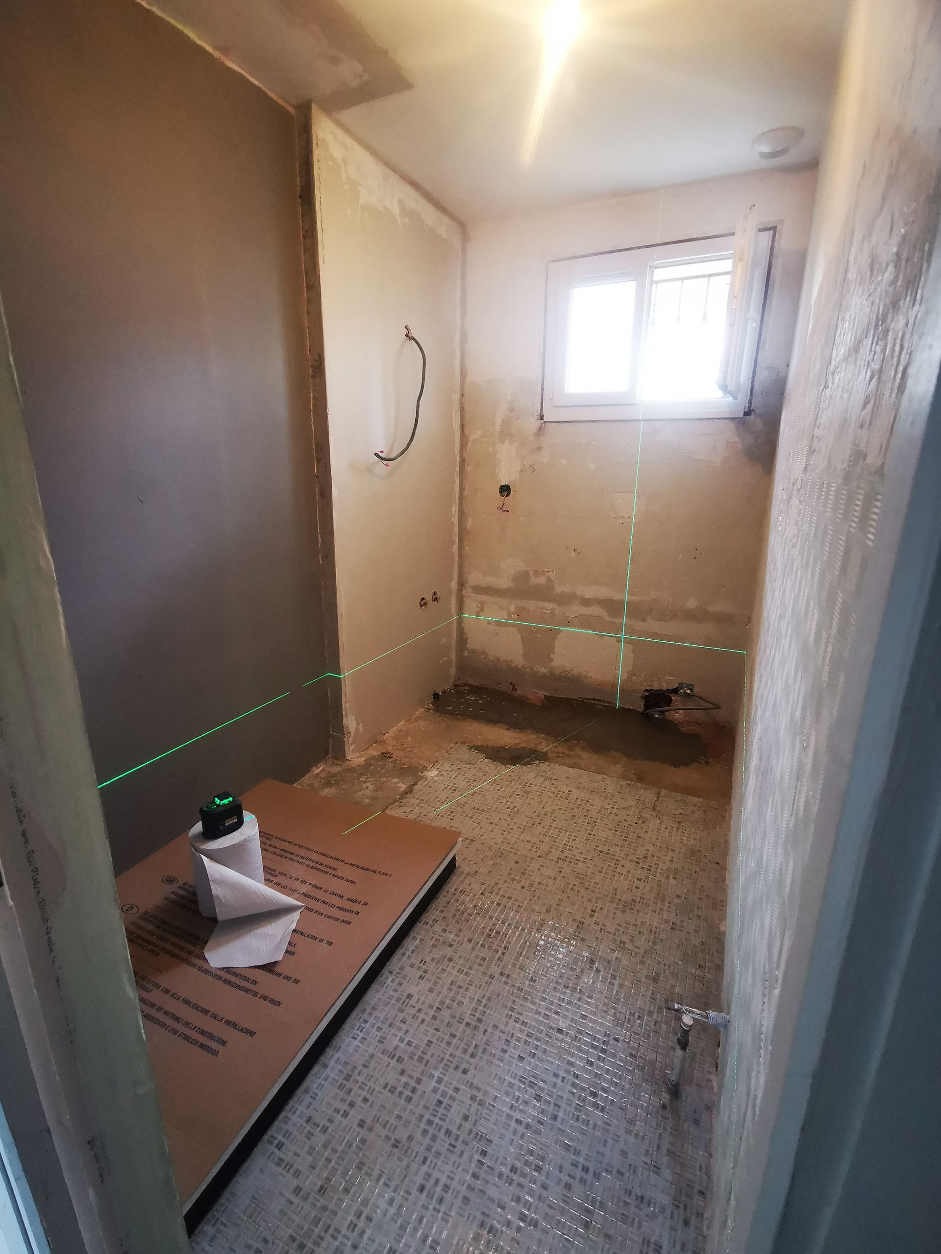 Salle de bain en construction avec murs bruts, plomberie apparente, niveau laser.