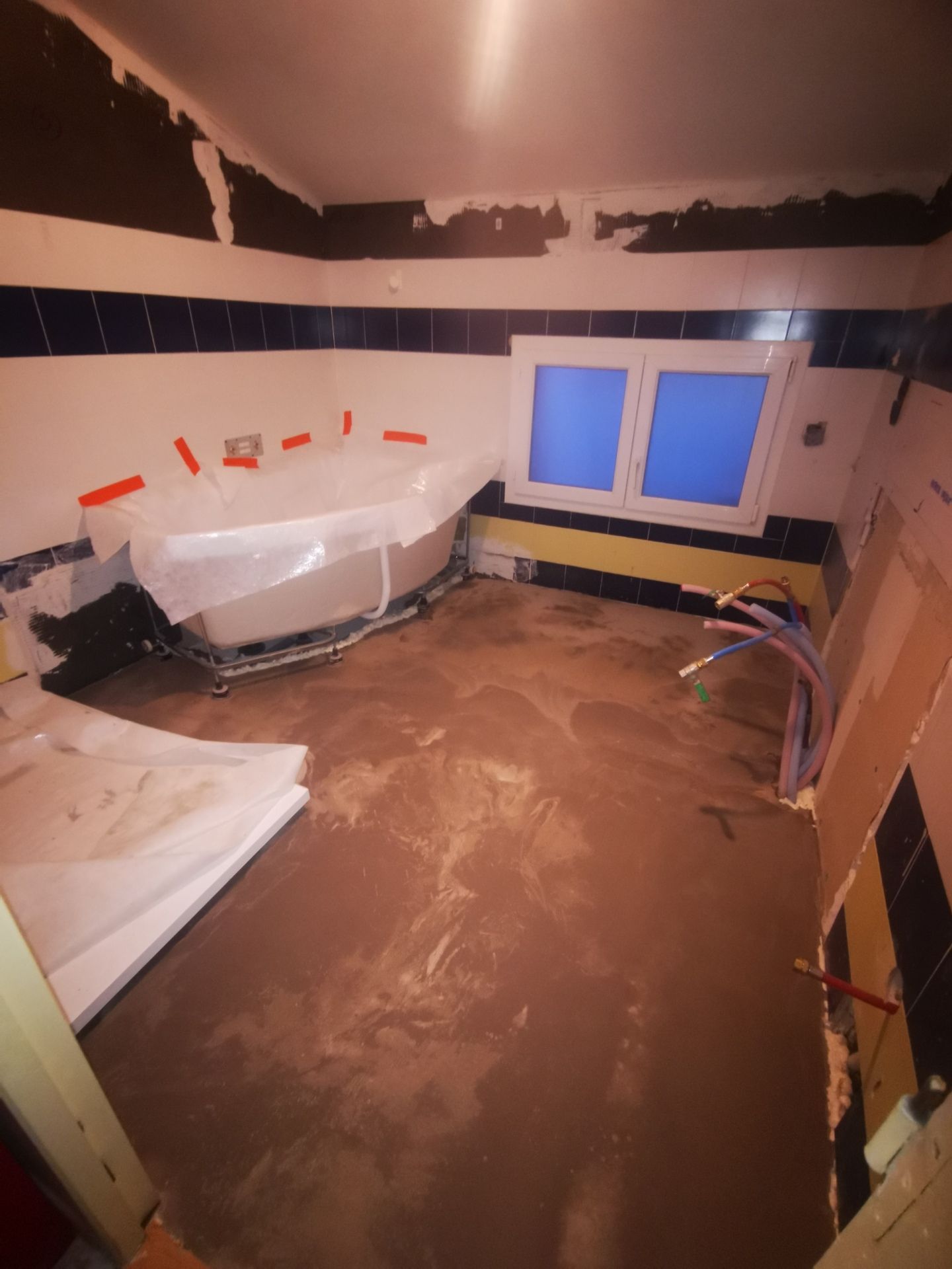 Salle de bain en rénovation avec baignoire recouverte de plastique, tuyaux apparents et murs non finis.