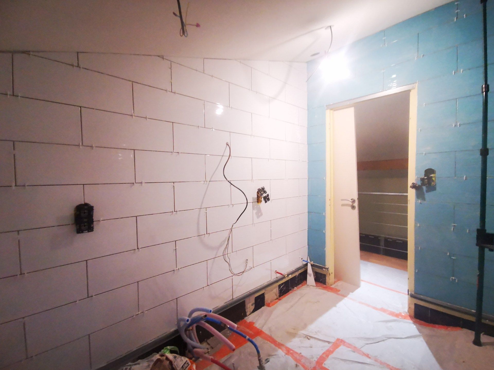 Salle de bain en construction; murs carrelés blancs, mur d'accent bleu, porte ouverte.