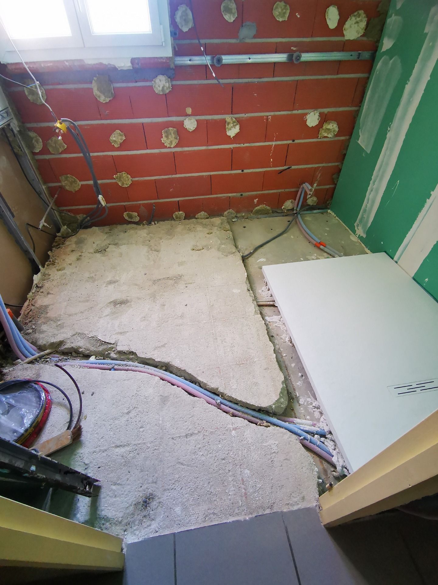 Chantier avec mur de briques apparentes et sol en béton, câblage électrique apparent.
