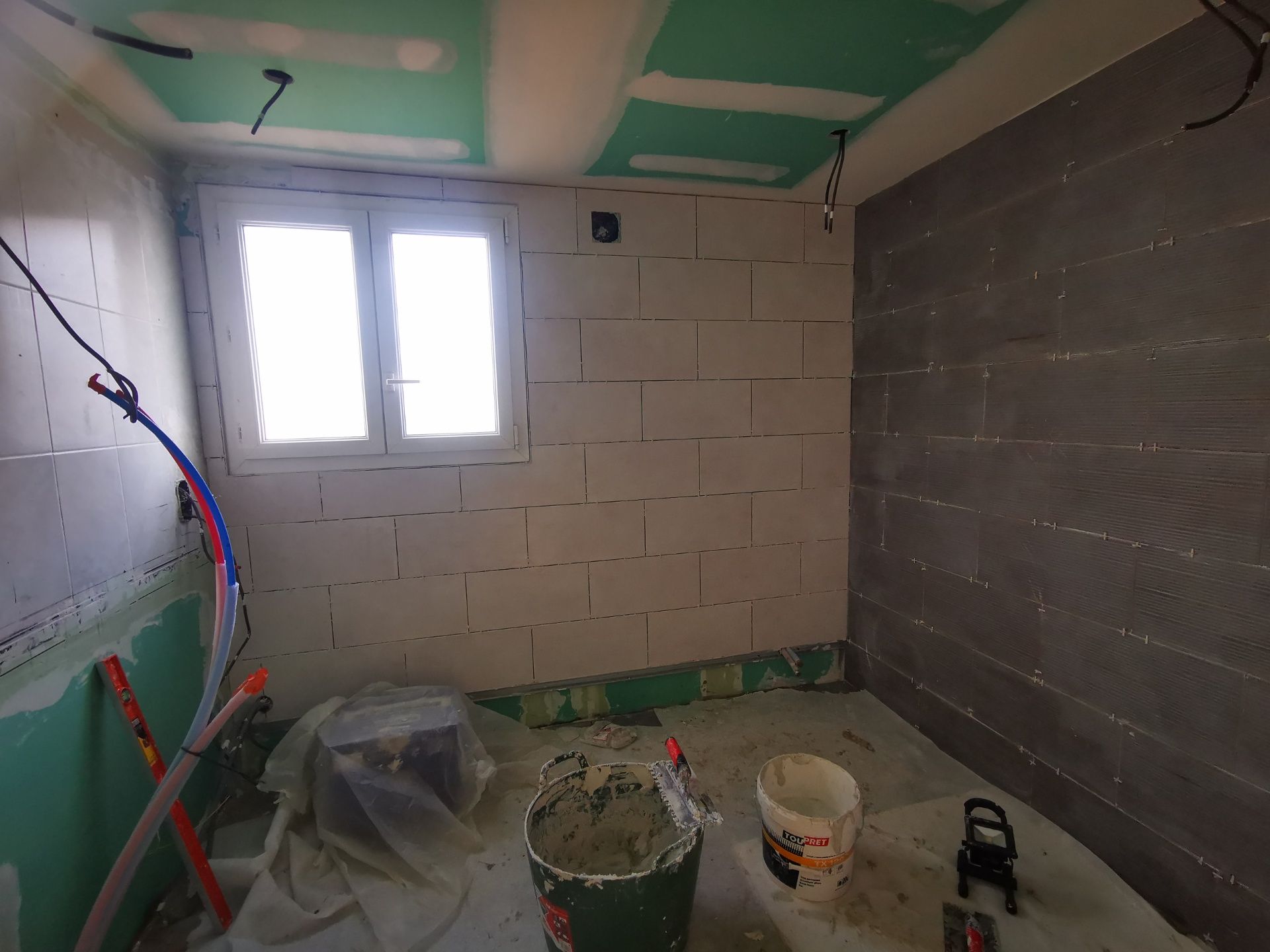 Intérieur de chantier avec murs bruts, une fenêtre et des outils au sol.