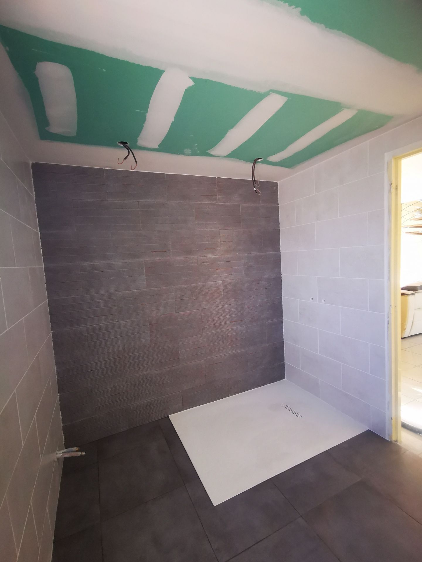 Rénovation de salle de bain : murs en carrelage gris, mur d'accent foncé, bac à douche, plafond exposé et porte.
